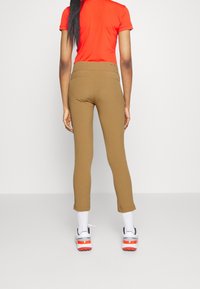 Pantalones marrones ajustados con cintura alta y detalles de costuras, combinados con una camiseta roja y zapatillas blancas con detalles en naranja.