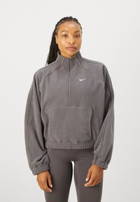 Szary polarowy pulower z wysokim kołnierzem, pół-zamkiem błyskawicznym i kieszenią z przodu. Posiada elastyczne mankiety i subtelne kontrastowe przeszycia. Logo Nike na klatce piersiowej.