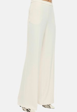 Pantaloni bianchi a vita alta e gamba larga abbinati a scarpe a punta con motivo in pelle di serpente su una modella.