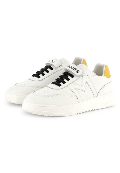 Sneaker bianche in pelle con lacci neri, linguetta grigia e accentatura gialla sul tallone. Presentano una punta perforata e una suola bianca spessa.
