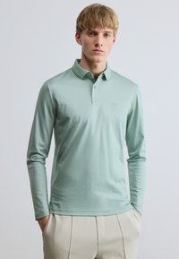 Hosszú ujjú, világos menta zöld sz�ínű, puha anyagból készült póló, kétgombos plisszével és apró logóval a mellkason.