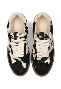 Sneakers con motivo di pelle di mucca, caratterizzati da un mix di materiale simile a pelliccia bianca e nera, lacci crema e suole in gomma marrone chiaro, dal design minimalista.