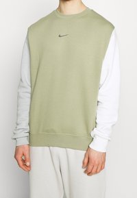 Man som bär en tvåfärgad sweatshirt med ljusgrön framsida och vita ärmar, med en liten svart Nike swoosh-logotyp på bröstet.
