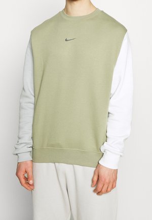 Homme portant un sweat-shirt bicolore avec un devant vert clair et des manches blanches, arborant un petit logo swoosh noir de Nike sur la poitrine.