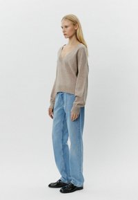 Pulover bej cu decolteu în V, cu manșete cu nervuri, asortat cu blugi lejerați, albastre deschise, și pantofi negri. Textură moale, croi lejer și design minimalist.