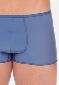 Herrenunterwäsche in taillierter Form, in einfarbigem Blau, aus einem glatten, elastischen Stoff gefertigt. Verfügt über einen stützenden Frontbeutel und unaufdringliche Nähte an den Kanten.