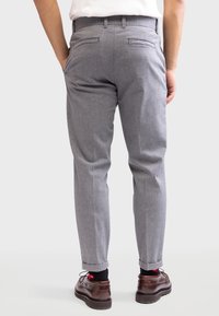 Grijze, taps toelopende broek met een gestructureerd patroon, voorzien van twee achterzakken en een opgerolde zoom. Gecombineerd met donkere leren schoenen.