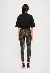 Black cropped t-shirt, loose fit, paired with form-fitting leggings featuring a dark, textured pattern with metallic accents. High-heeled shoes.