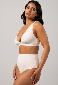 Trådlös bh och högmidjade underkläder i ljus beige. Slät tygkvalitet, djup V-ringning och minimala detaljer i hårdvara.