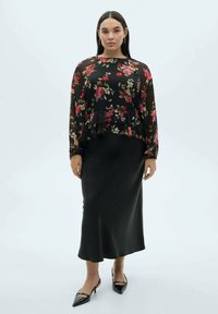 Blusa floreale nera con maniche lunghe, design a strati, abbinata a una gonna nera liscia. Gli accessori includono orecchini a cerchio e scarpe a punta.