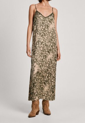 Kvinde iført ærmeløs olivengrøn maxikjole med beige blomster- og uglemønster, kombineret med tanfarvede ruskind ankle-støvler.