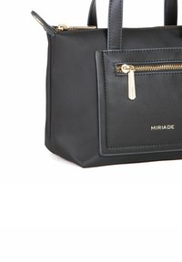 Sort håndtaske lavet af glat syntetisk materiale, med en lynlåslomme, guld hardware detaljer, korte håndtag og en rektangulær form.