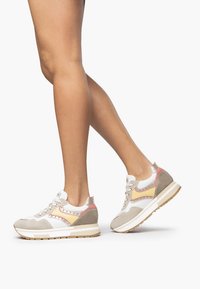 Zapatillas para mujer con ante beige, malla blanca y acentos rosa, con una suela de goma texturizada y tachuelas decorativas.