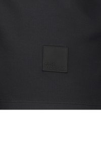 Schwarzer Stoff-Patch mit geprägt "Jack Wolfskin" Logo, rechteckige Form, glatte Textur, Teil eines größeren Textilprodukts.