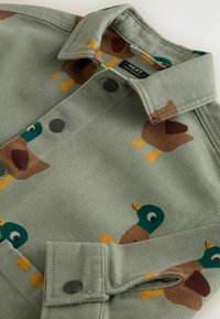 Light green jacket with snap buttons featuring a pattern of brown and green cartoon ducks with yellow feet.