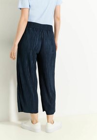 Marineblauwe geplooide cropped broek met eenelastische tailleband, gecombineerd met witte sneakers, met een gladde textuur en subtiele verticale strepen.