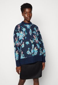 Jersey azul marino con un colorido estampado floral en rosa y azul. Presenta un escote acanalado y mangas largas, combinado con una falda negra.