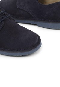 Scarpe di camoscio blu navy con punta arrotondata, cuciture tono su tono e suola in gomma blu chiaro, caratterizzate da un classico design con lacci e accenti minimali.