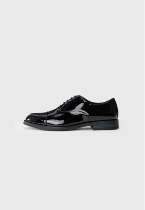Black patent leather dress shoe with a round toe, subtle brogue details, and a smooth finish. Features a low-profile rubber sole and lace-up design.
