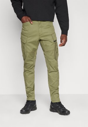 Pantalons cargo olive avec de multiples poches, coupe cintrée, détails de couture et genoux renforcés, assortis à des baskets noires.
