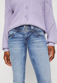 Light purple knitted sweater with three buttons, paired with light blue denim jeans featuring front pockets and a faded wash.