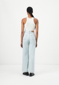Jeans de pierna ancha de un azul claro con cintura alta, cinco bolsillos y parche de cuero en la parte trasera, combinados con una camiseta ajustada blanca y zapatos negros.