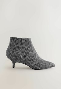 Spids-tå ankelstøvle lavet af sort og hvid herringbone-stof med en strømlinet silhuet og en lav kitten heel.