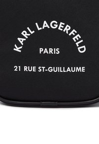 Un materiale nero testurizzato presenta del testo bianco in rilievo, "KARL LAGERFELD PARIS 21 RUE ST-GUILLAUME," in un design curvo.