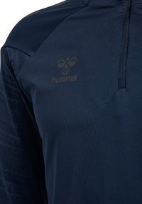 Pull-over de sport bleu marine avec fermeture éclair quart de zip et logo hummel noir sur la poitrine gauche, manches texturées et à motifs.