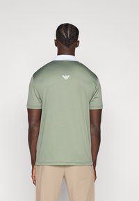 Πόλο πουκάμισο σε ελιά πράσινο με λευκό γιακά, κοντά μανίκια και διακριτικό λογότυπο στο πίσω μέρος. Λεία υφή, χαλαρή εφαρμογή.