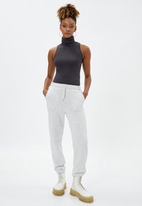 Pantalones de chándal grises con cintura elástica y bolsillos laterales, combinados con un ajustado suéter sin mangas de cuello alto oscuro. Botas gruesas blancas con cordones.
