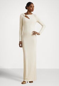 Vestido bodycon em creme com mangas compridas, decote assimétrico com recorte e detalhe dourado, silhueta até ao chão.