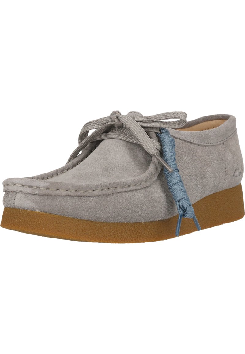 Zapato de ante gris con punta redondeada, suela de goma y cordones gris claro. Presenta un acento azul en el cordón, textura suave y diseño sencillo.