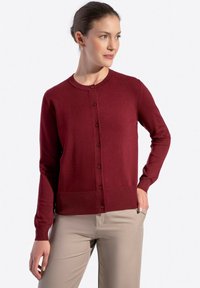 Cardigan bordeaux con scollo rotondo, maniche lunghe e chiusura con bottoni. Presenta una texture liscia e un motivo a maglia uniforme. Abbinato a pantaloni beige.