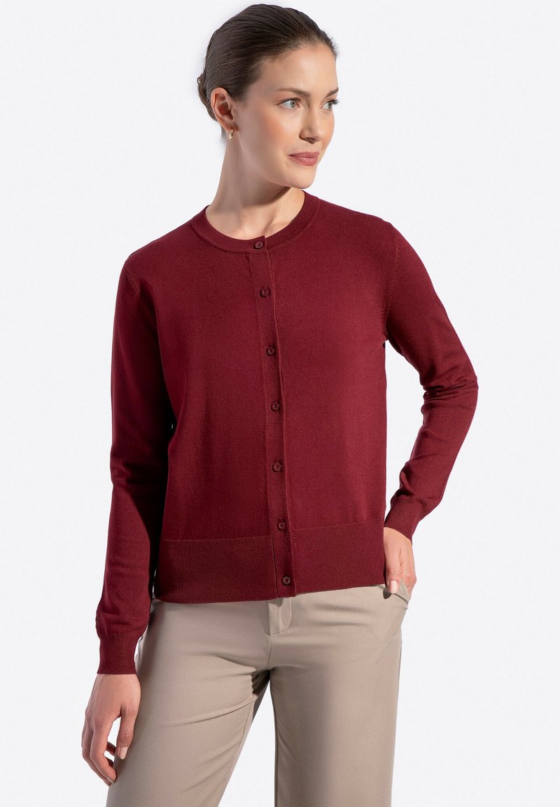 Cardigan bordeaux con scollo rotondo, maniche lunghe e chiusura con bottoni. Presenta una texture liscia e un motivo a maglia uniforme. Abbinato a pantaloni beige.