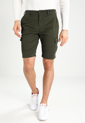 Shorts cargo vert foncé en coton avec poches latérales, un devant plat et une fermeture éclair. Portés avec des chaussures de sport blanches.
