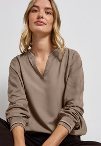 Pull marron avec un col en V et des manches froncées. Le tissu est doux avec une texture lisse, présentant des poignets rayés en contraste.