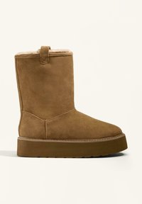 Brown suede ankle boot with a soft fur lining, flat sole, and a rear tab for easy wear. Features reinforced stitching along the seams.