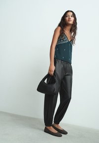 Teal top s uskim naramenicama i uzorkom na izrezu, crne hlače od umjetne kože s elastičnim manžetama, teksturirana crna torba i balerinke s ukrasnim zakovicama i špicastim vrhom.