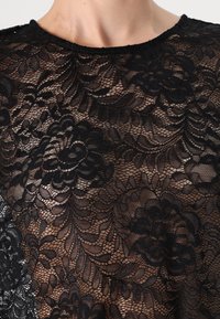 Black lace top featuring floral patterns, intricate textures, and a round neckline. The fabric is sheer and delicate with a light, flowing design.
