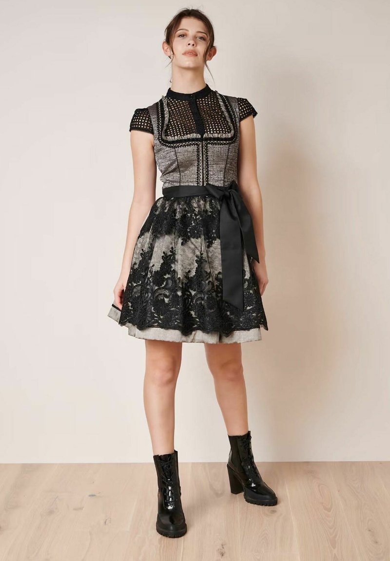 Schwarz-graues Kleid mit einem strukturierten Oberteil, Spitzenakzenten am Rock und einem Satinband in der Taille. Glänzende schwarze Knöchelstiefel runden den Look ab.