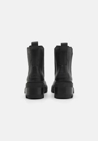 Black leather ankle boots with a smooth texture, elastic side panels, and a sturdy platform sole. Features logo accents on the back.