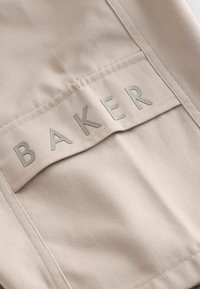 Tissu beige à surface texturée, avec une poche cousue sur laquelle est embossé "BAKER" en gris clair. Design épuré et moderne.