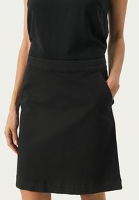 Zwarte katoenen rok met een rechte snit, zijzakken en een tailleband. Heeft een afwerkingssteek aan de zoom voor extra detail.