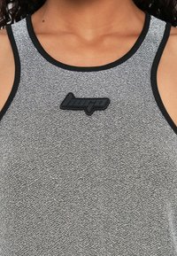 Débardeur de sport gris en tissu texturé, avec des bords noirs et un logo noir embossé sur le devant.