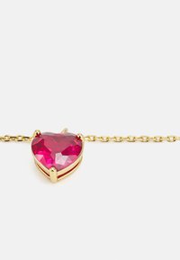 Gold chain necklace featuring a heart-shaped, faceted pink gemstone, set in a four-prong setting. Chain has a delicate link design.