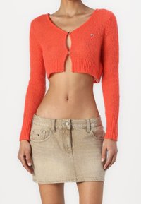 Koralowy krótki sweter dzianinowy z długimi rękawami, z zapinaniem na guziki z przodu. Połączony z jasnobeżową mini spódnicą jeansową o subtelnej fakturze.