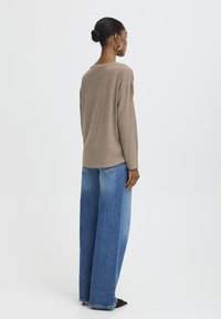 Beigen Langarmoberteil mit lockerer Passform, kombiniert mit blauen Jeans im Wide-Leg-Schnitt. Das Material wirkt weich mit einer subtilen Textur.
