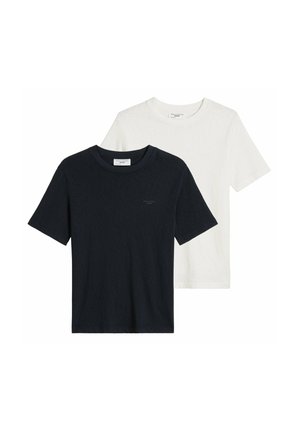 Homme portant un t-shirt blanc uni manches courtes, jean bleu clair, collier chaîne argentée et bracelet argenté, main dans la poche, torse visible.