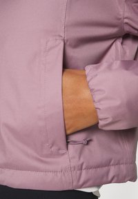 Ljuslila jacka med en slät, texturerad finish. Inkluderar en sidoficka och elastiska ärmslut för justerbar passform.